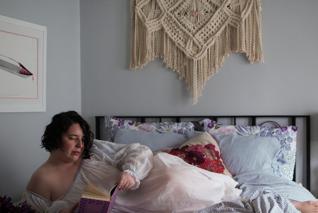 Model wearing handmade, sheer, intimate apparel laying in bed, reading a book, after a hysterectomy.