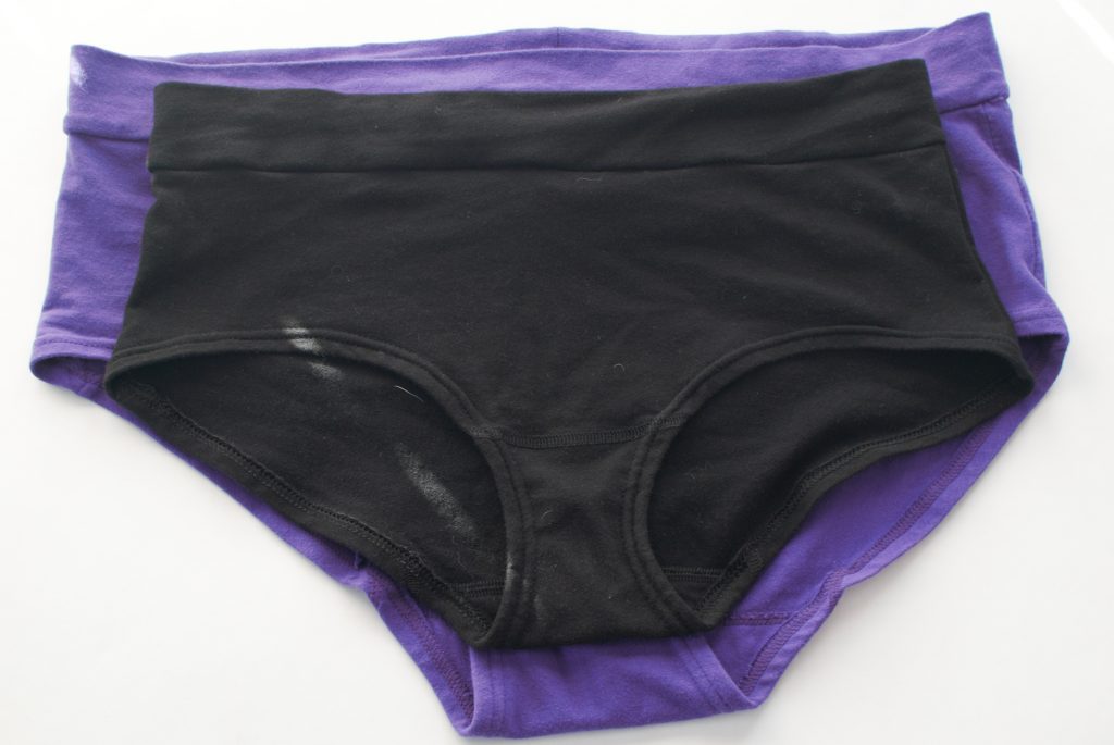 Size 1L Kate and Vos Classics brief in purple and Signature brief in black. Purple briefs are visibly bigger than the black ones. 