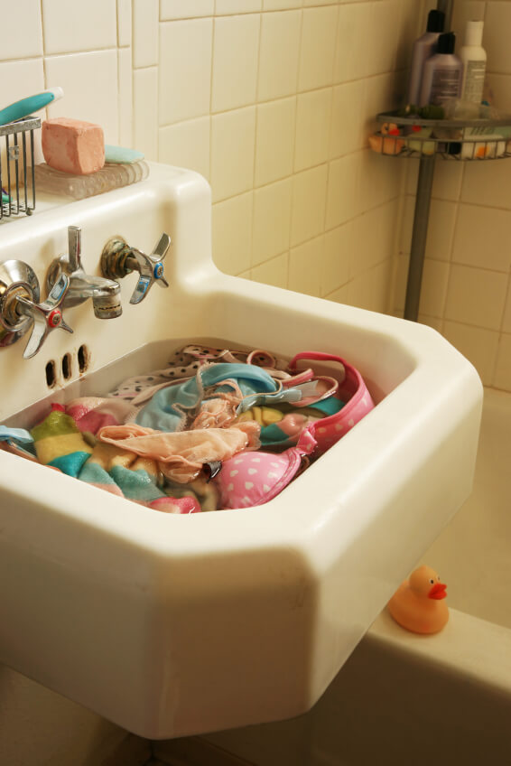 Sustainable lingerie soaking to wash in white, bathroom sink. Bathtub is visible.