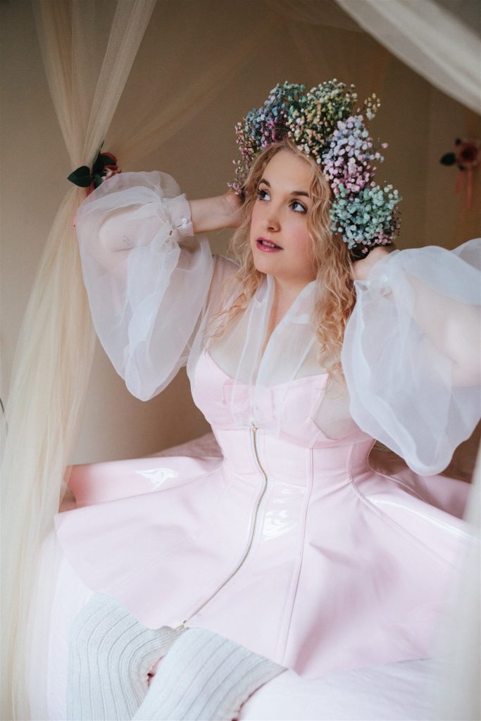 Model sitting wearing Artifice light pink PVC corset skirt. 