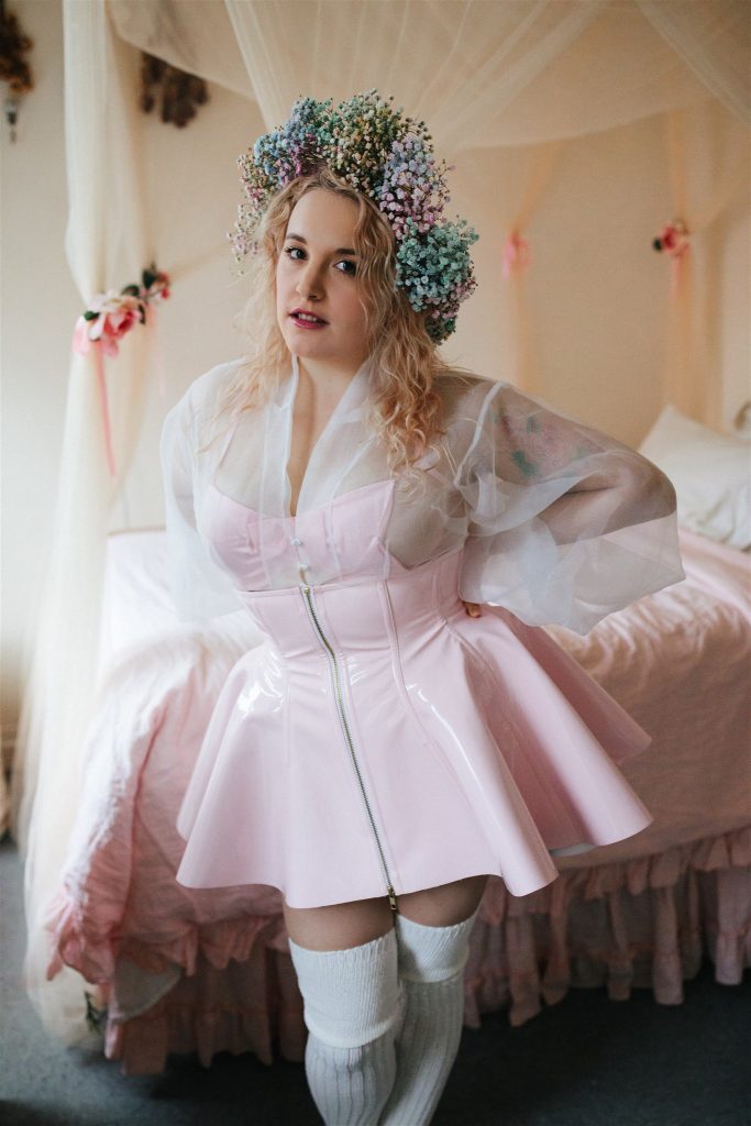 Model standing wearing Artifice, light pink PVC corset skirt.