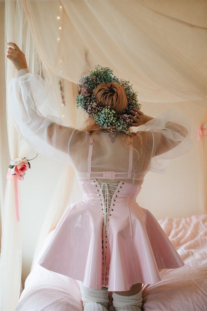 Back view of kneeling model wearing Artifice light pink PVC corset skirt.