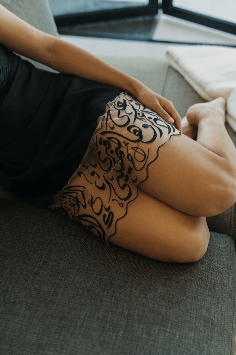Close up detail of hem of Hadal Lingerie love language robe dress. Black embroidered arabic calligraphy on sheer tulle. 