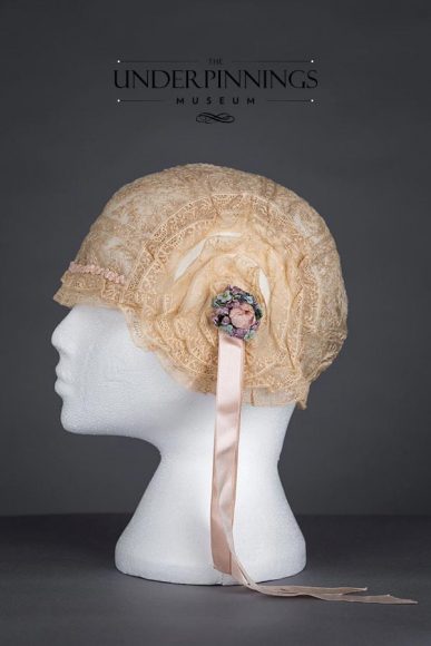 Embroidery and lace boudoir cap with rosettes and silk ribbon streamers. Estimated to be from the 1920s. From The Underpinnings Museum Collection. Photo by Tigz Rice Studios