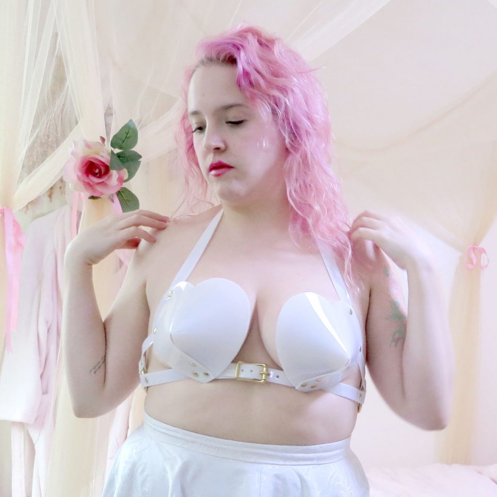 Model wearing Apatico white, PVC bullet bra. Shows where extensions of heart shaped cups dig into skin slightly.