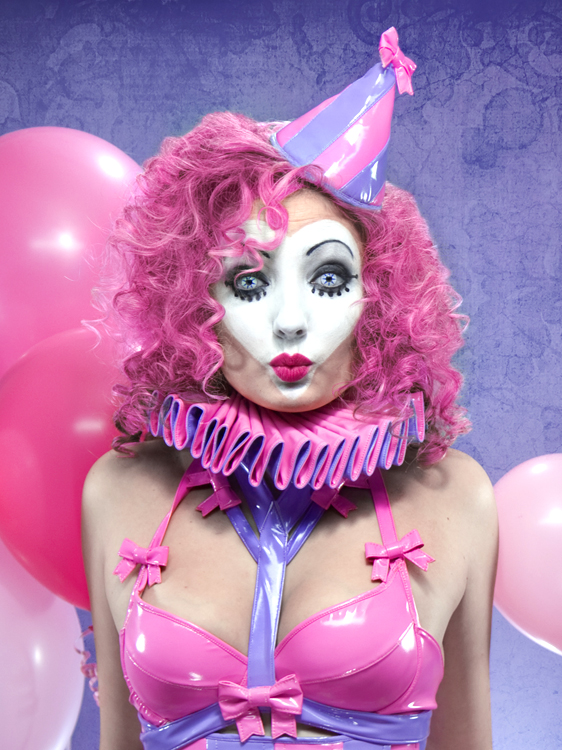 Artifice Clothing PVC Fetish Clown Costume. Purple and pink party hat, ruffle collar, pink bra with bows, and purple harness.