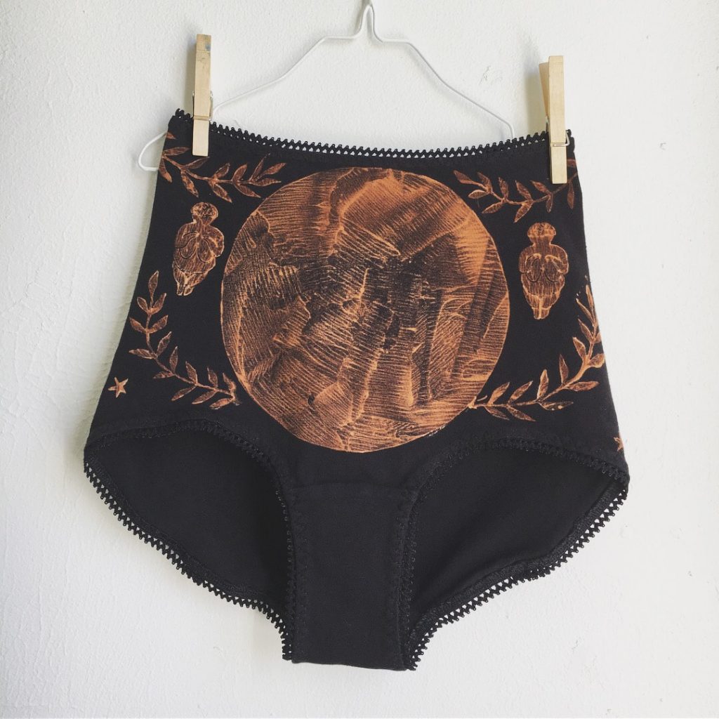 Close up of Serpent & Bow, high cut, black Venus brief featuring moon and goddess imagery on front.